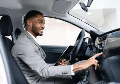 Car Dealer Sitting In Driver's Seat Checking Auto Wokring In Dealership Showroom During Automobile Exhibition. Selective Focus